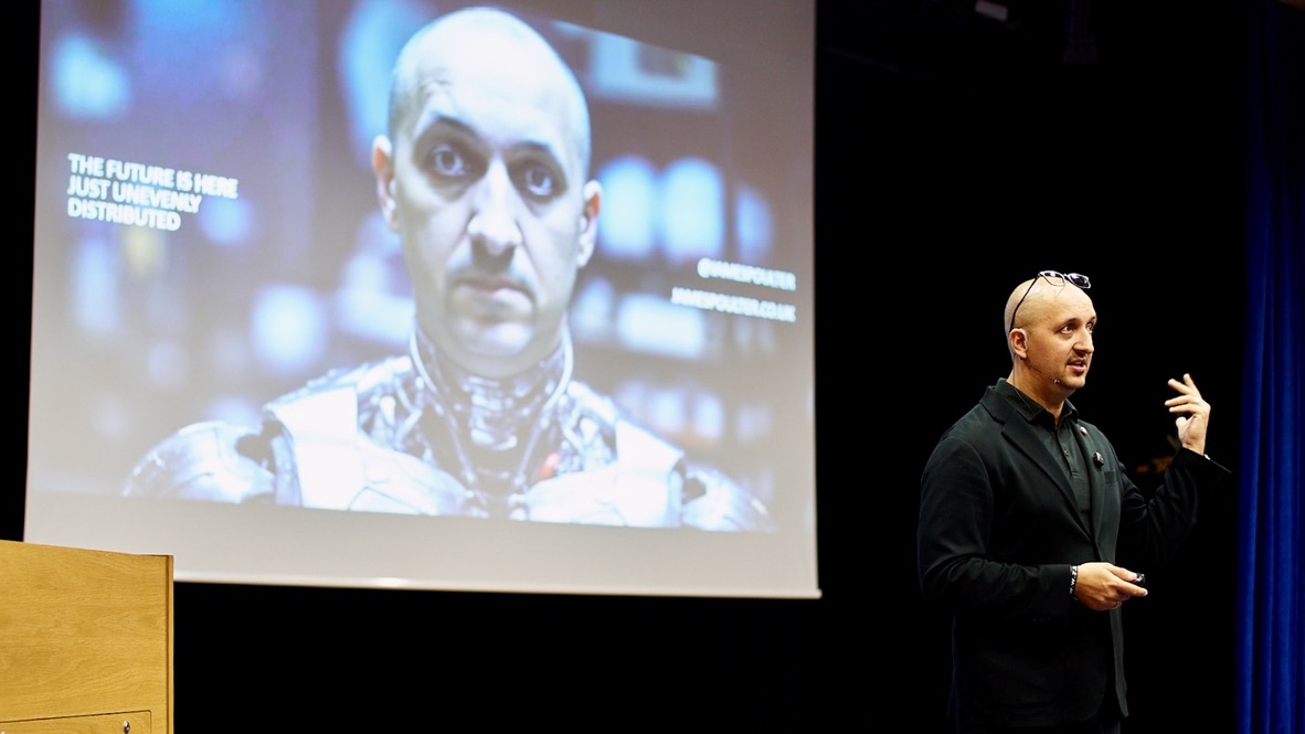 James Poulter delivering an AI keynote speech on stage with futuristic technology presentation