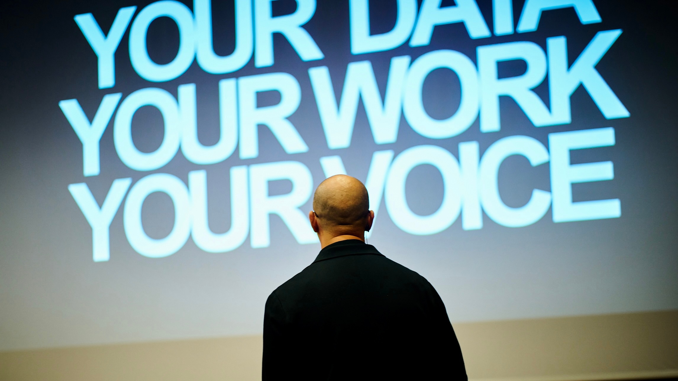 James Poulter presenting at a conference with YOUR DATA, YOUR WORK, YOUR VOICE on screen